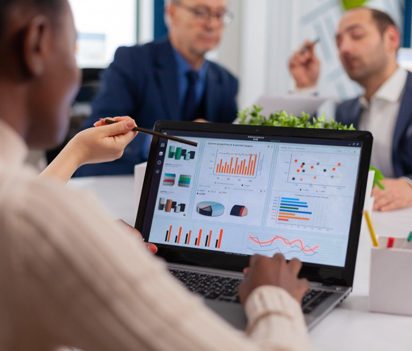 Une consultante est en train de présenter les étapes du projet à l'équipe  projet qui est assise autour d'une table en salle de réunion. 